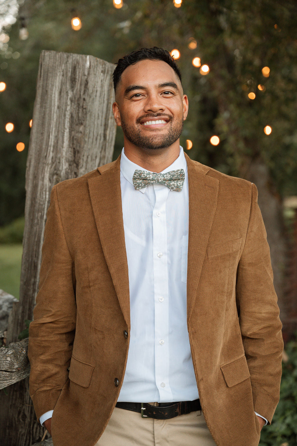 Men's pre-tied bow tie on model: green floral pattern with cream flowers and orange spots