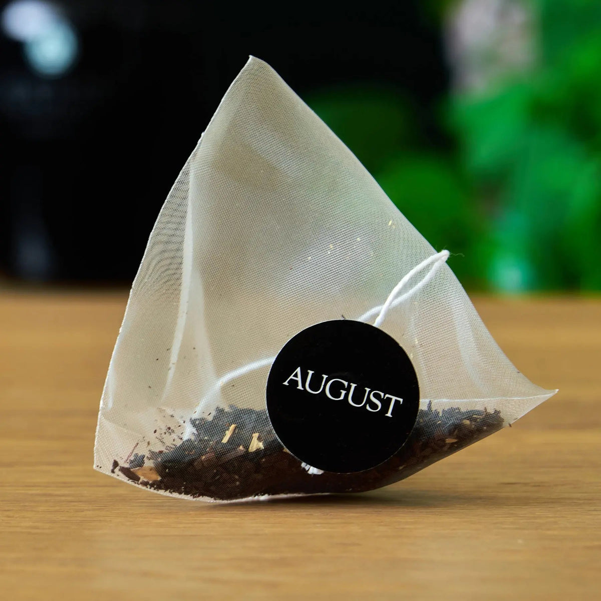 Pyramid tea bag filled with loose tea, with an August tag.