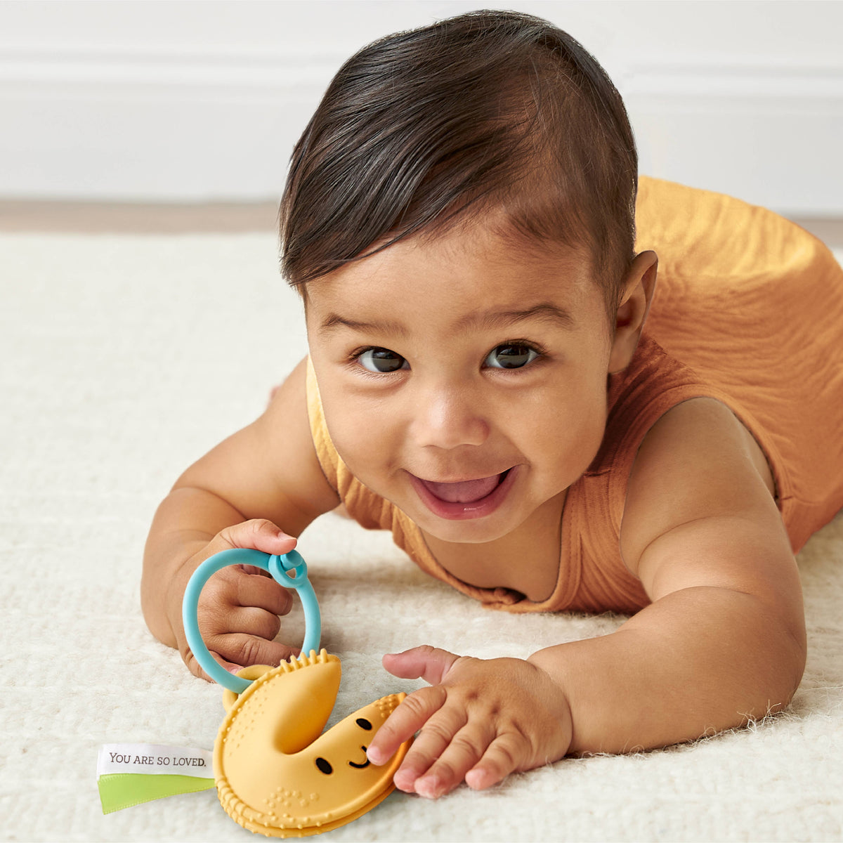 Baby crawling while playing with a fortune-cookie silicone teether and blue ring