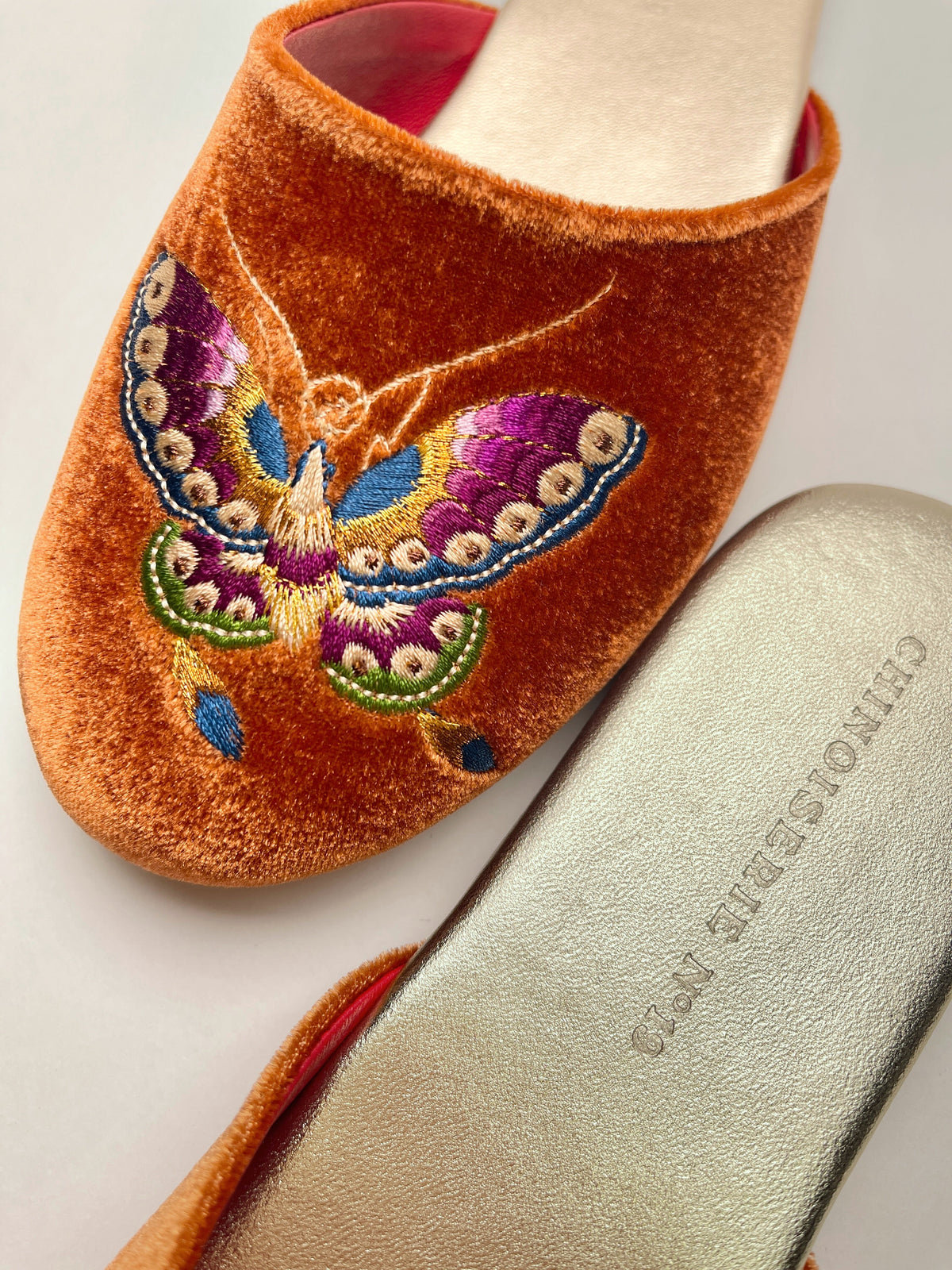 Close-up of burnt orange velvet mule with colorful butterfly embroidery on upper