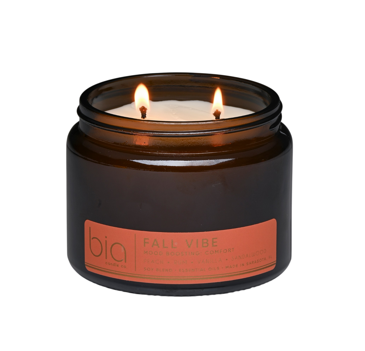 Amber soy candle jar with two lit wicks and orange label on the front