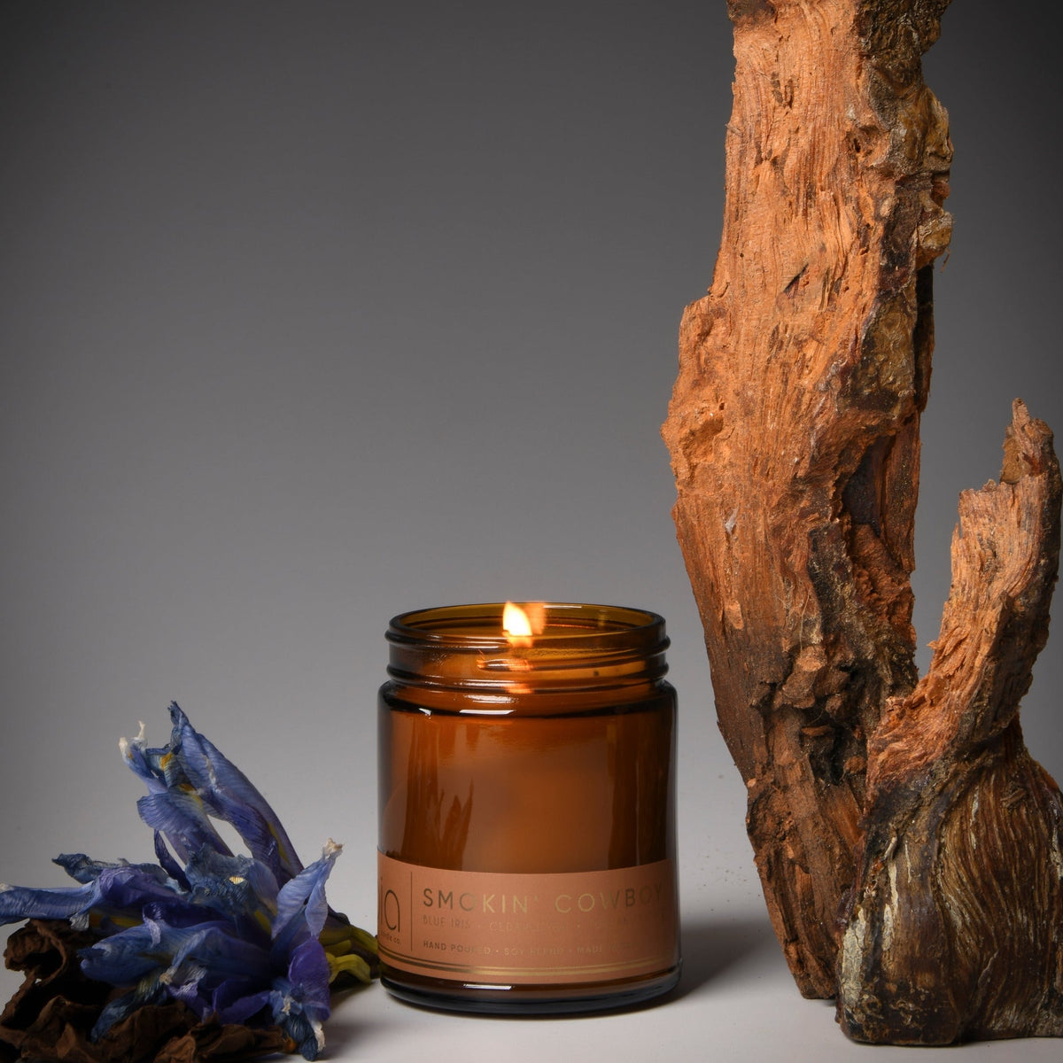 Amber glass soy candle jar with lit flame, dark lid, tan label