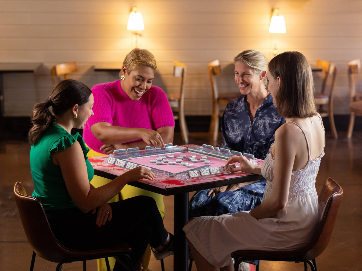Pink floral mahjong mat on table as players sit around arranging tiles