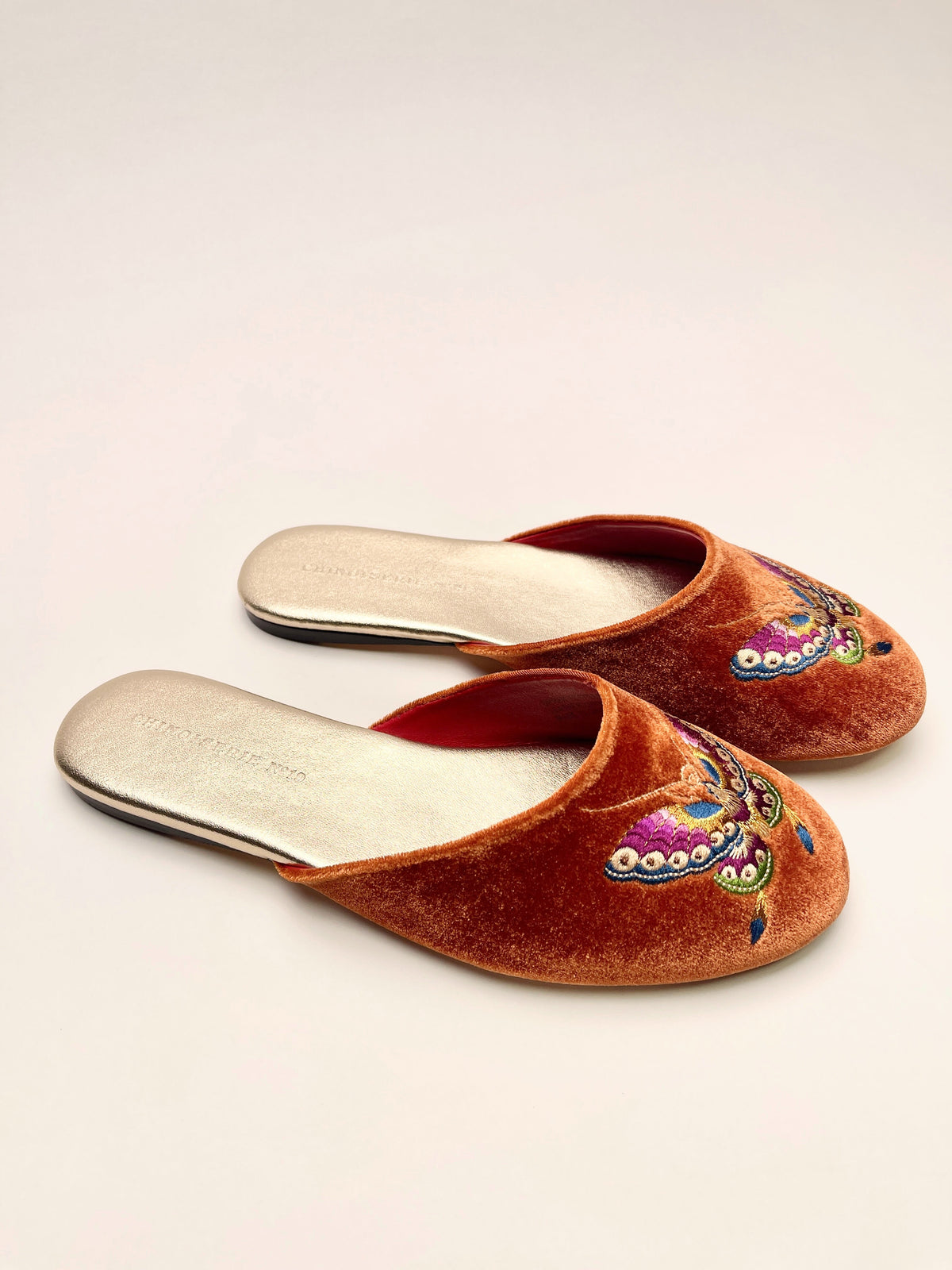 Burnt orange velvet mules with embroidered butterfly details on the toes