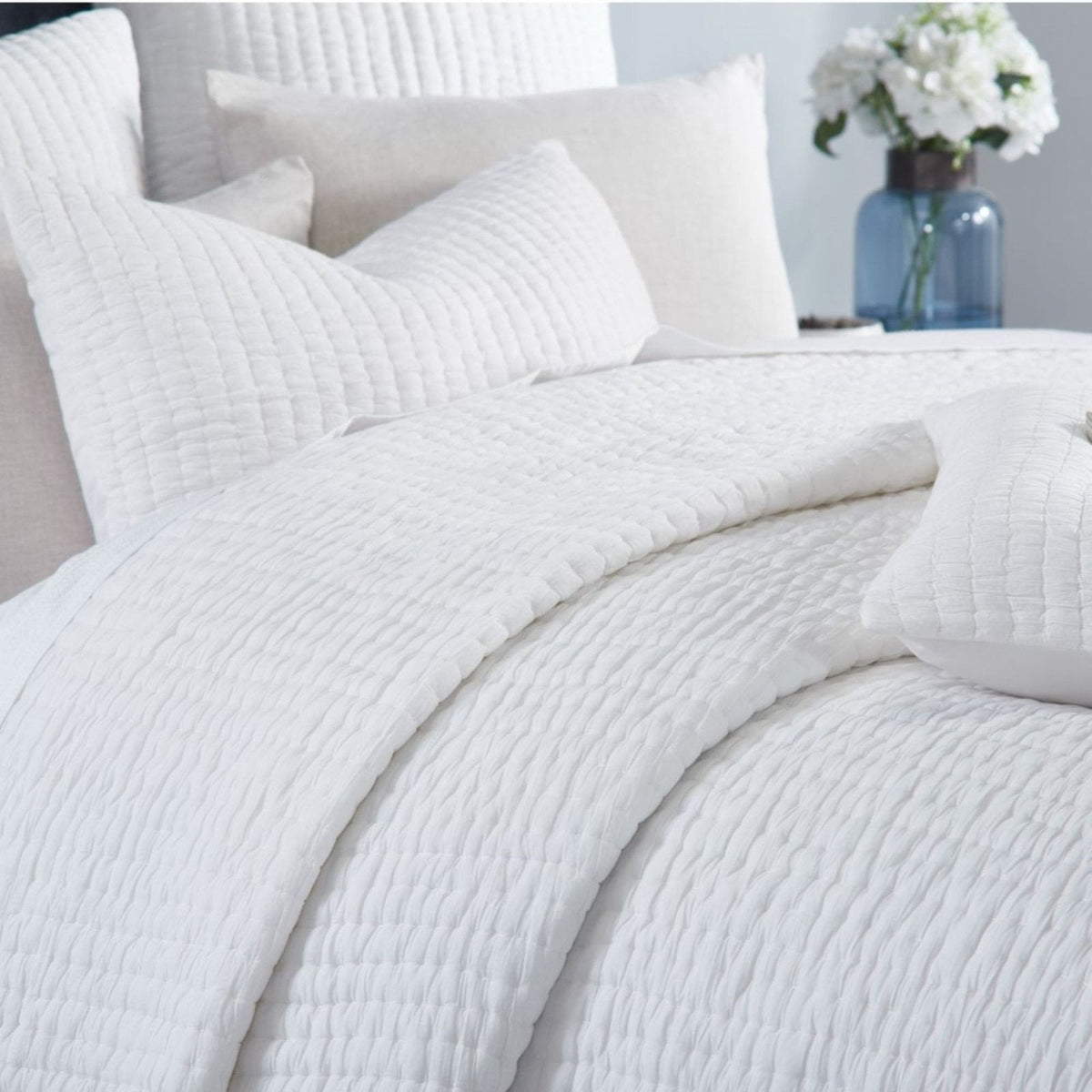 White washed-cotton quilt with textured stitched pattern, draped on a bed