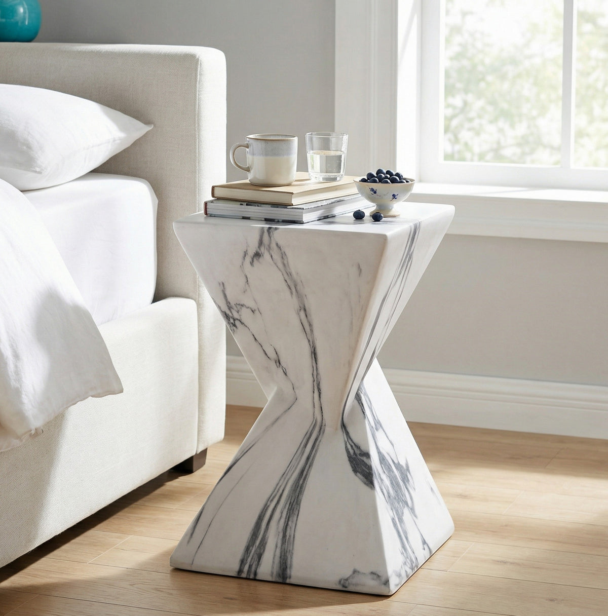 Hourglass-shaped concrete side table with a square top and gray veining beside a bed
