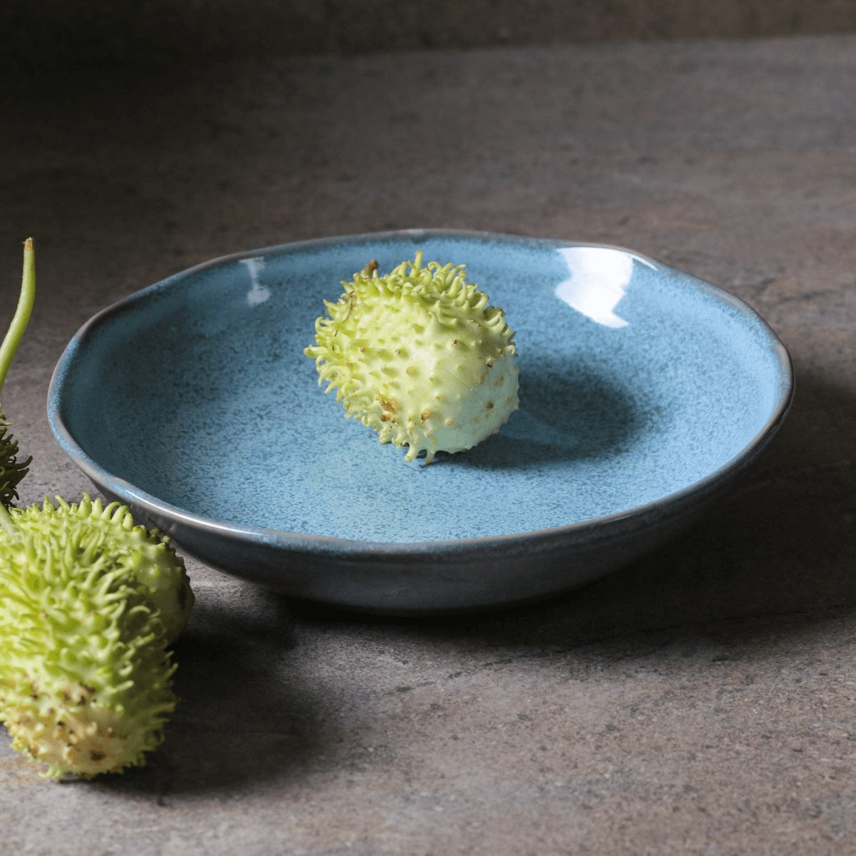 Blue speckled pasta plate with green garnish, shallow round serving bowl.