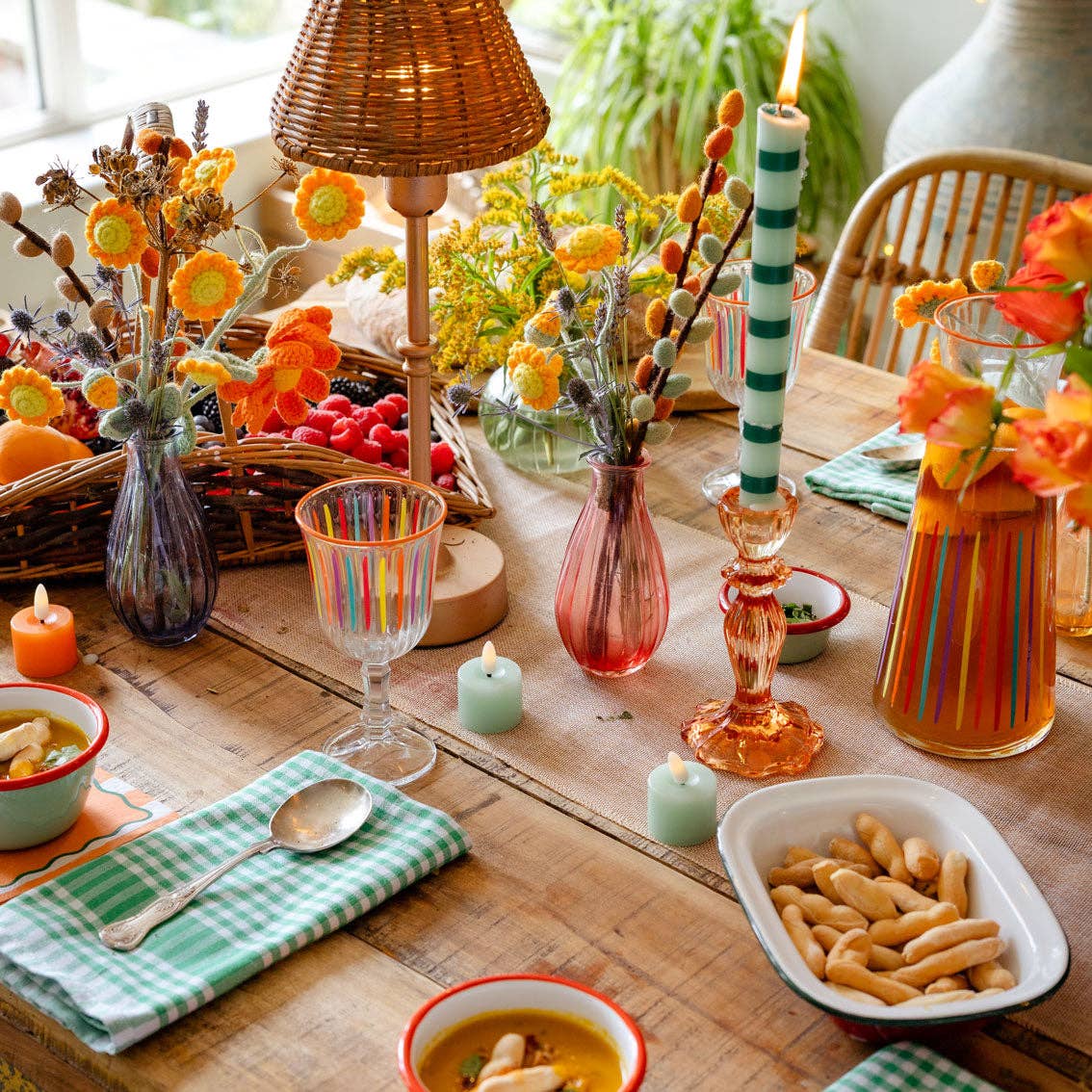 Tall green-and-white striped dinner candle with lit wick on table setting.