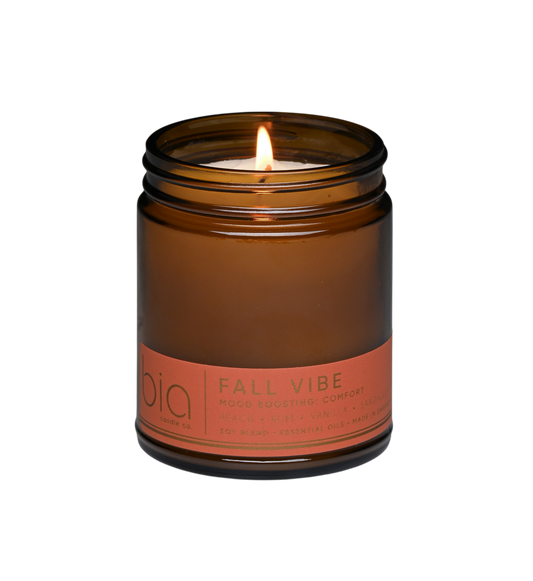 Amber soy candle in clear glass jar with lit wick and orange label band