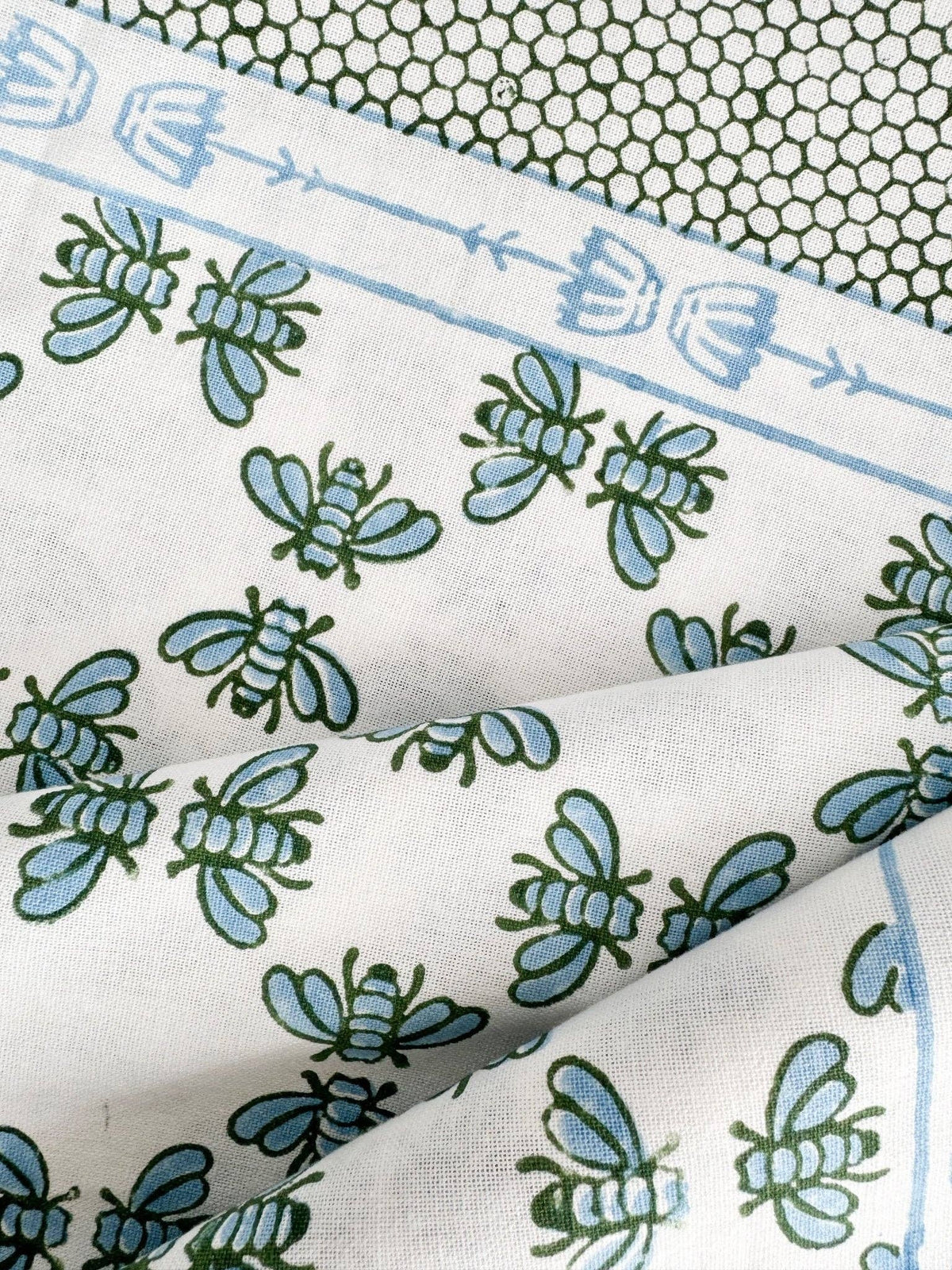 Table throw close-up of blue border icons and green floral motifs on white fabric.