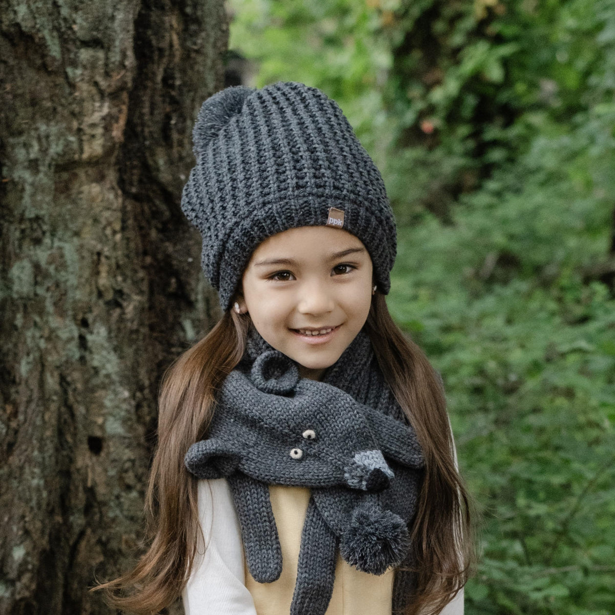 Dark gray knit beanie with pom-pom and folded ribbed cuff, worn by a child