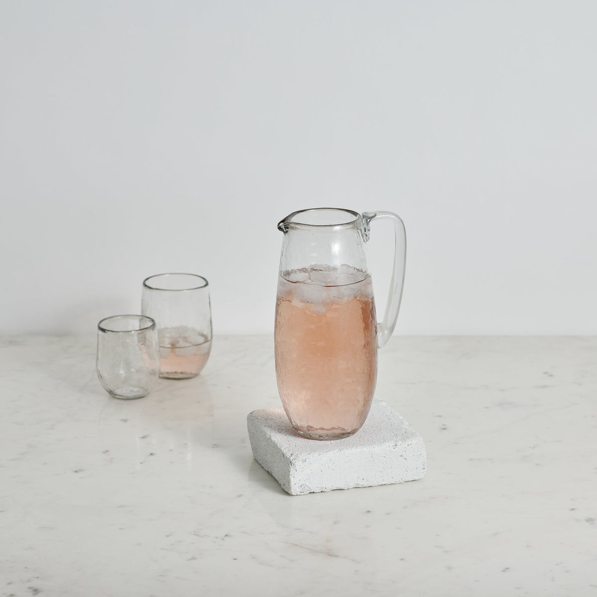 Pebbled glass pitcher with handle on gray speckled base, filled with pale pink drink