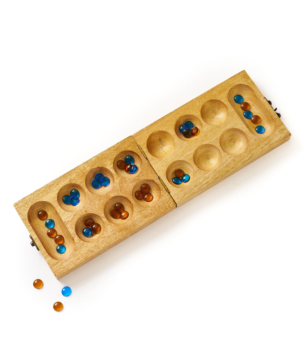 Carved wooden Mancala board with circular wells and scattered blue and amber stones