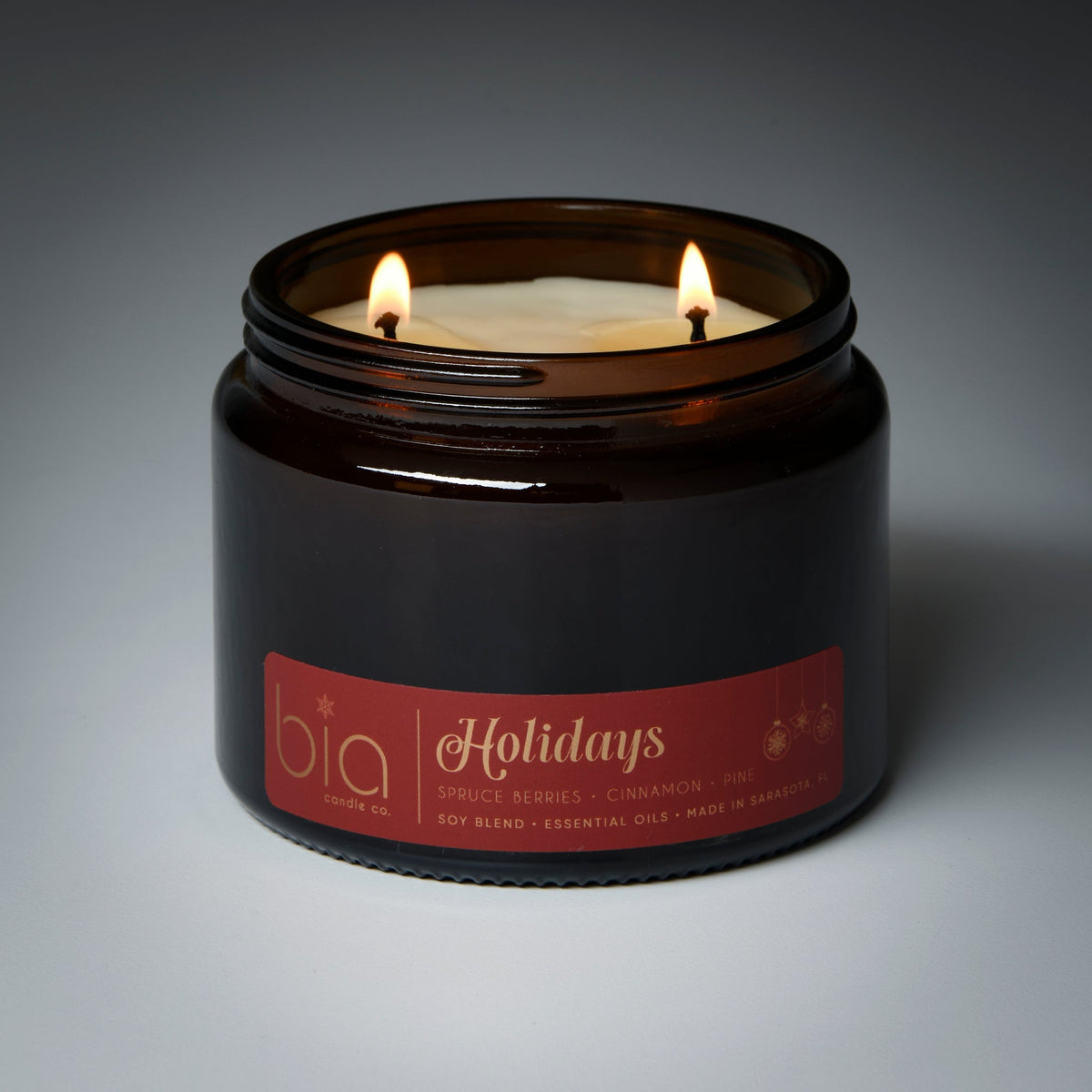 Amber glass candle jar with two lit flames and “Holidays” label