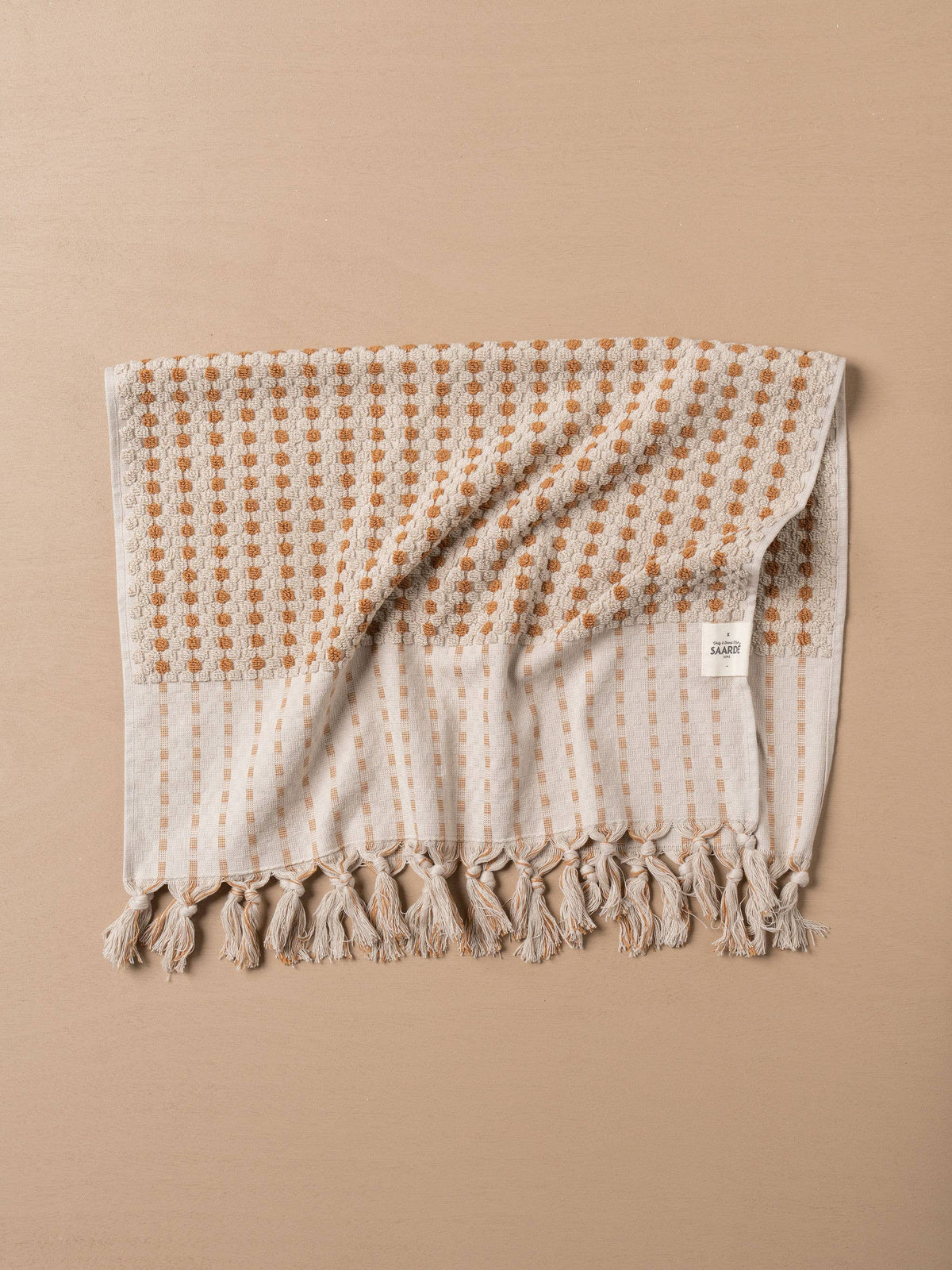 Turkish hand towel folded with terracotta dotted grid, stone panel, and tasselled hem