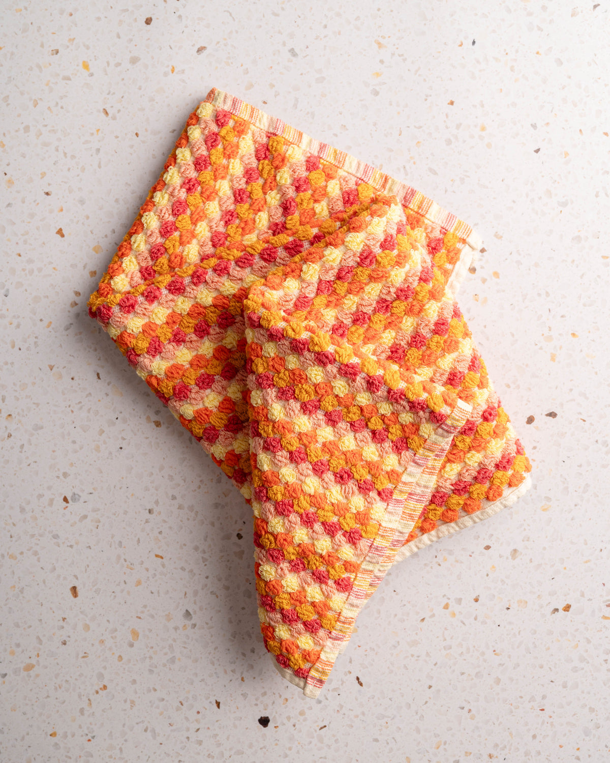Checkered hand towel in coral, orange, and cream tones, no tassels, folded diagonally.