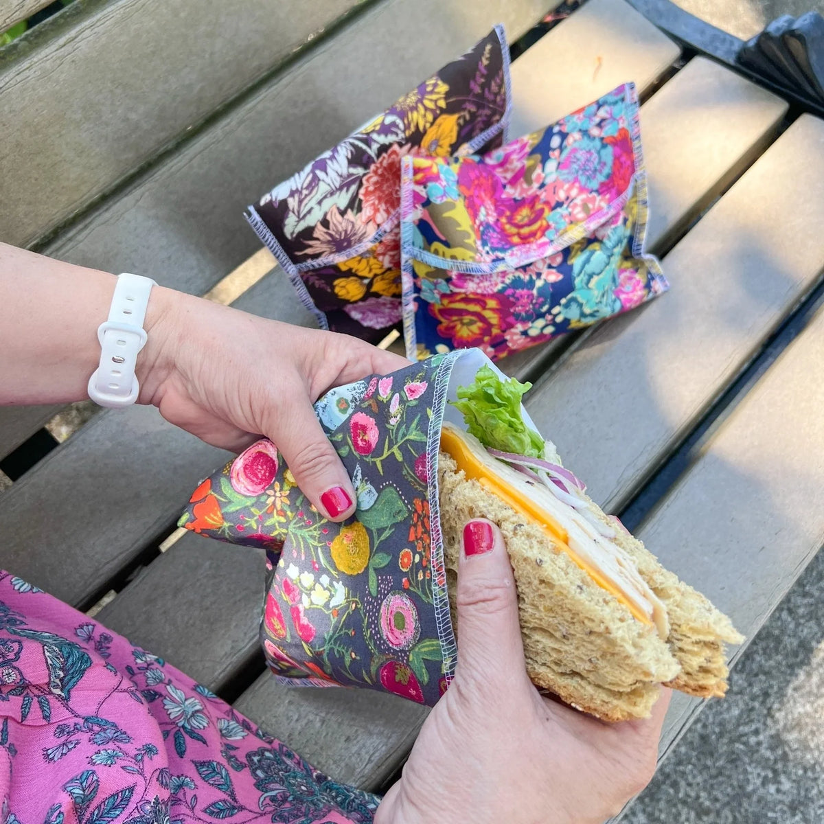 Reusable snack bag with colorful floral print, held open with sandwich pieces inside
