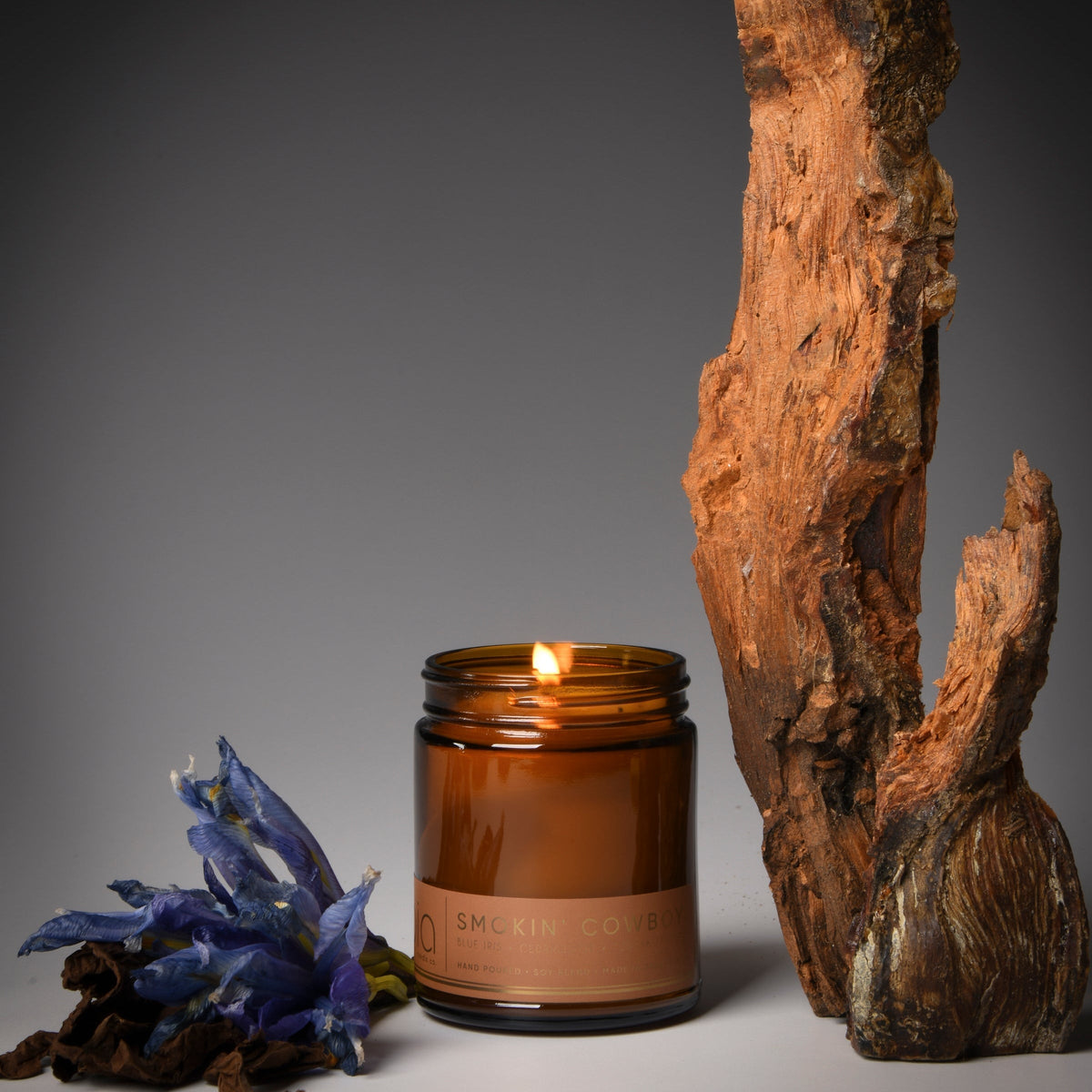Amber glass soy candle jar with lit flame and tan label