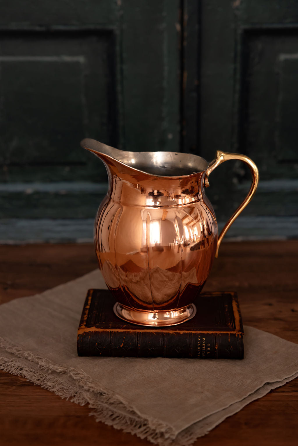 Copper metal pitcher with curved handle and flared spout, close angled view.