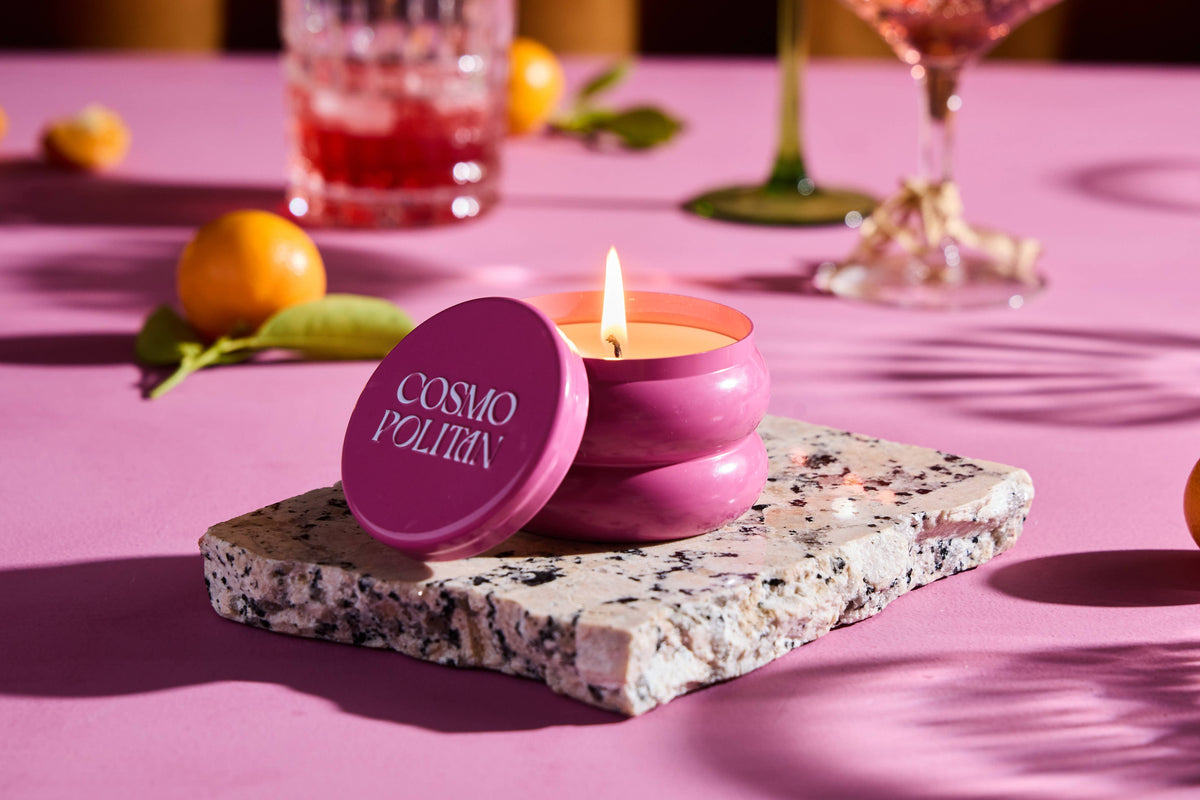 Rewined Cosmopolitan candle in a pink glass jar with a matching lid and a lit wick.
