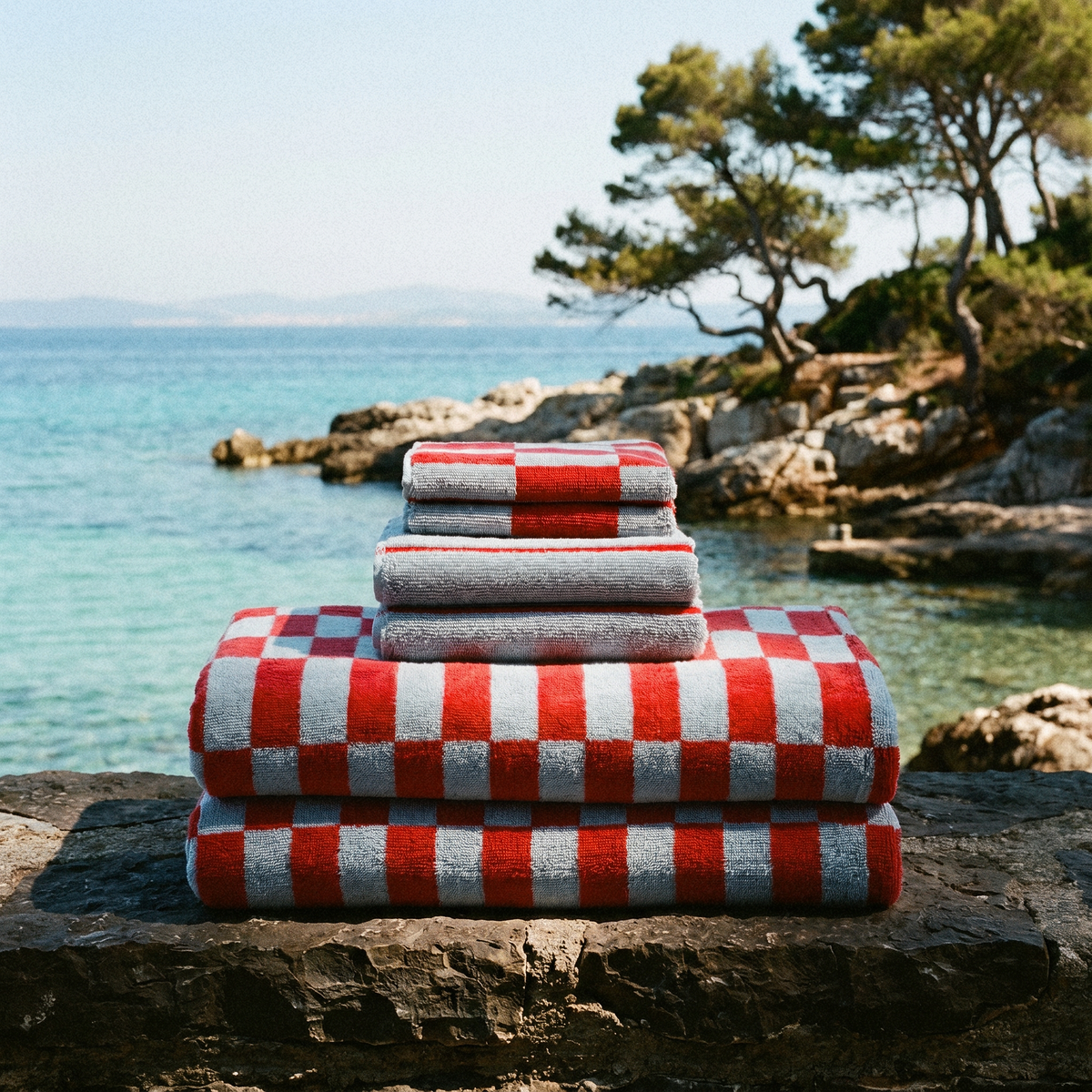 Folded gray towels and red-and-white check towels stacked on a seaside rock