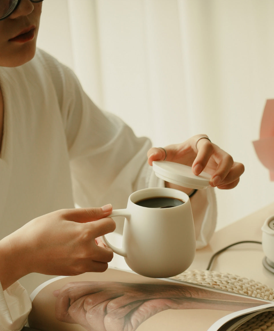 Off-white self-heating mug held as a hand pours hot drink into the cup