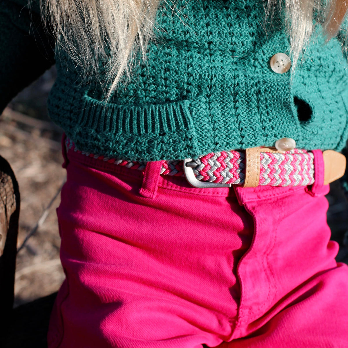 Pink, gray, and white braided stretch belt with tan leather details, worn with pink pants