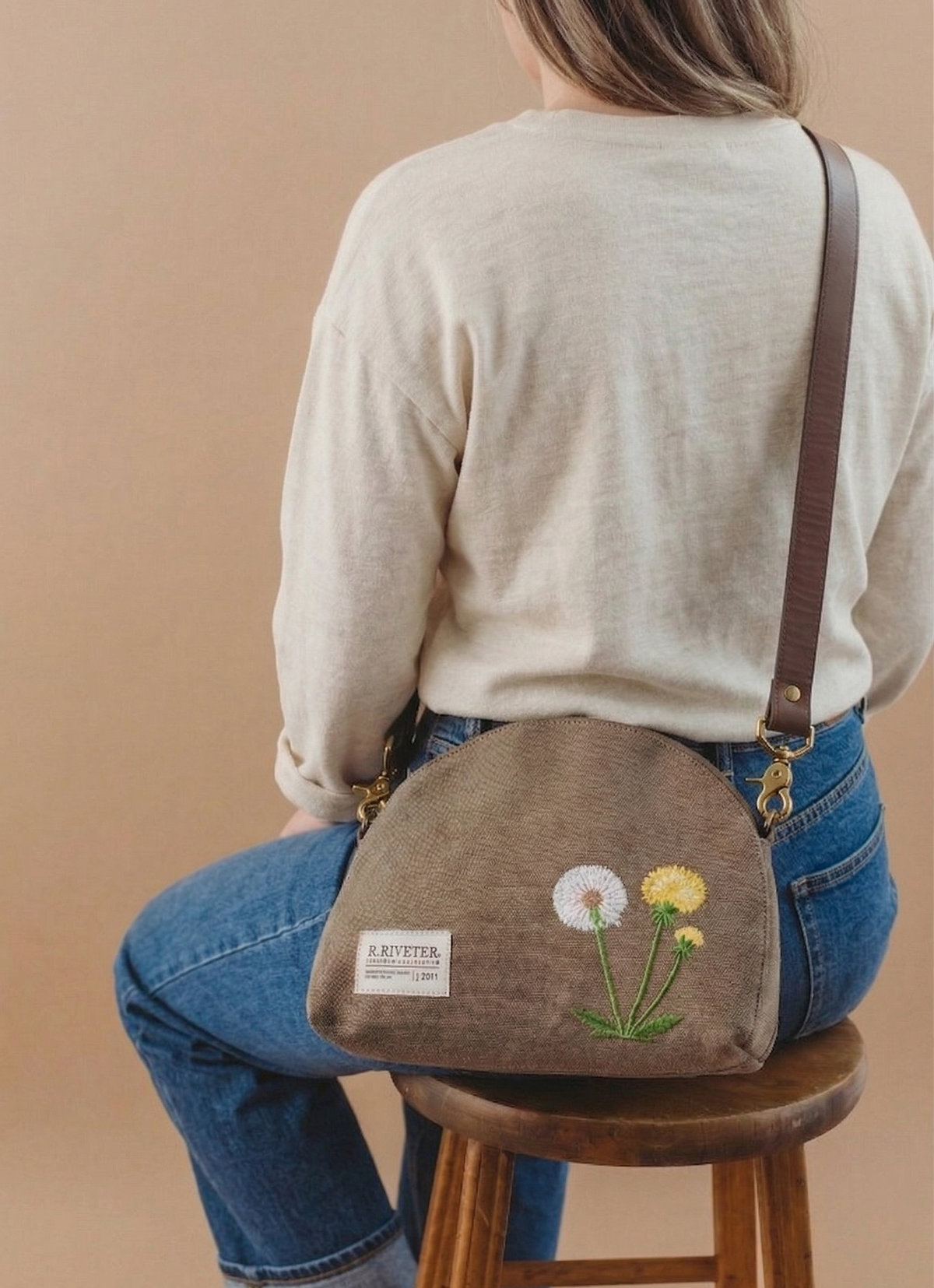 Small canvas crossbody bag with floral embroidery, worn on back with leather strap