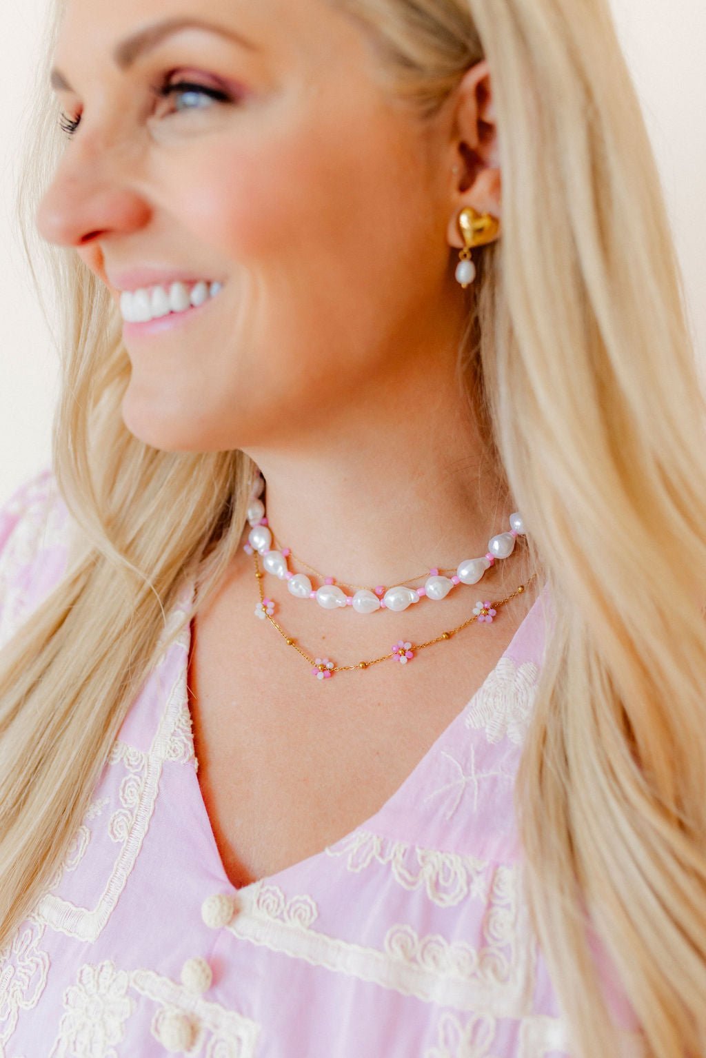Gold-tone heart drop earrings with pearl bead dangles on ear.