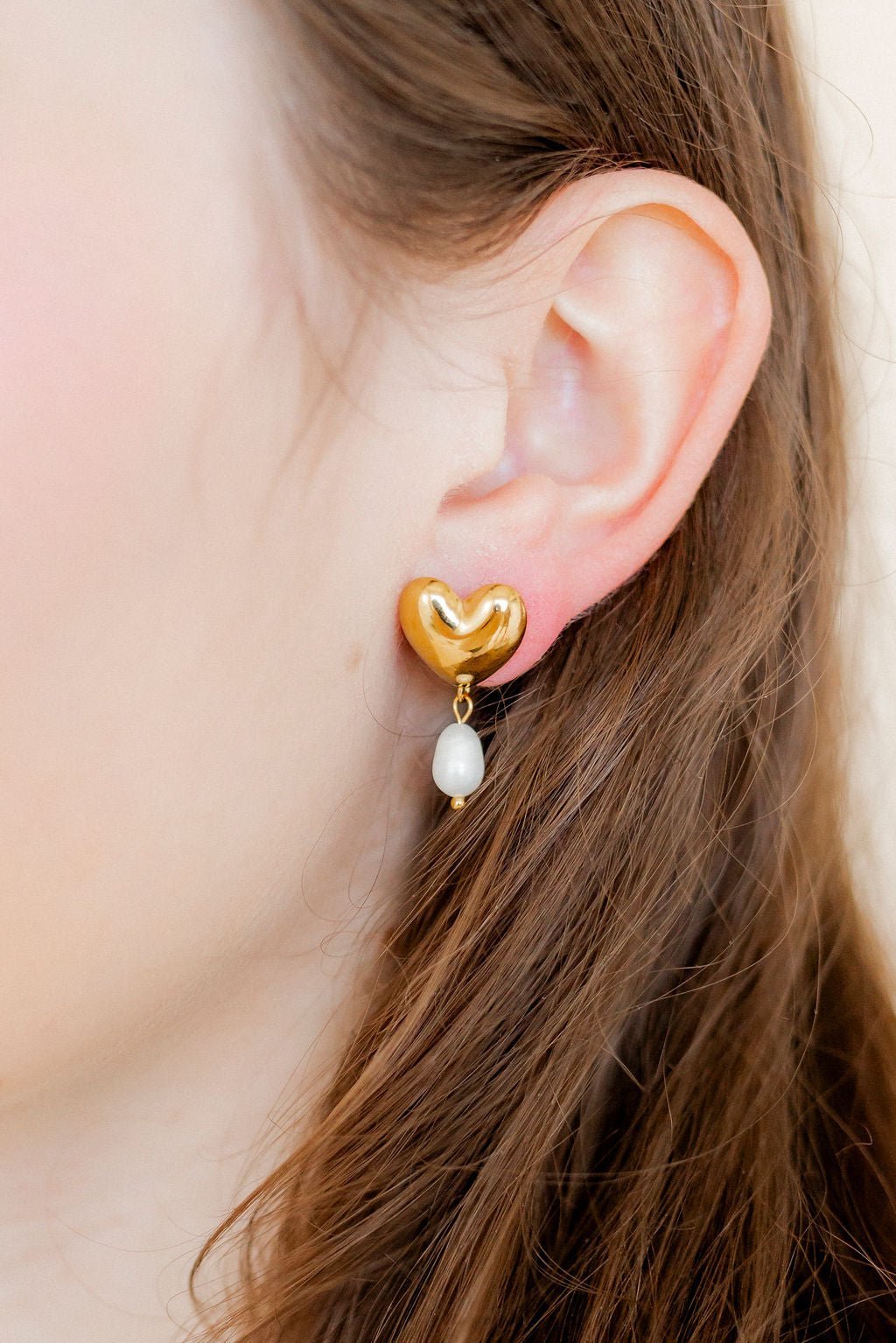 Gold-tone heart drop earrings with pearl bead dangles, close-up on ear.