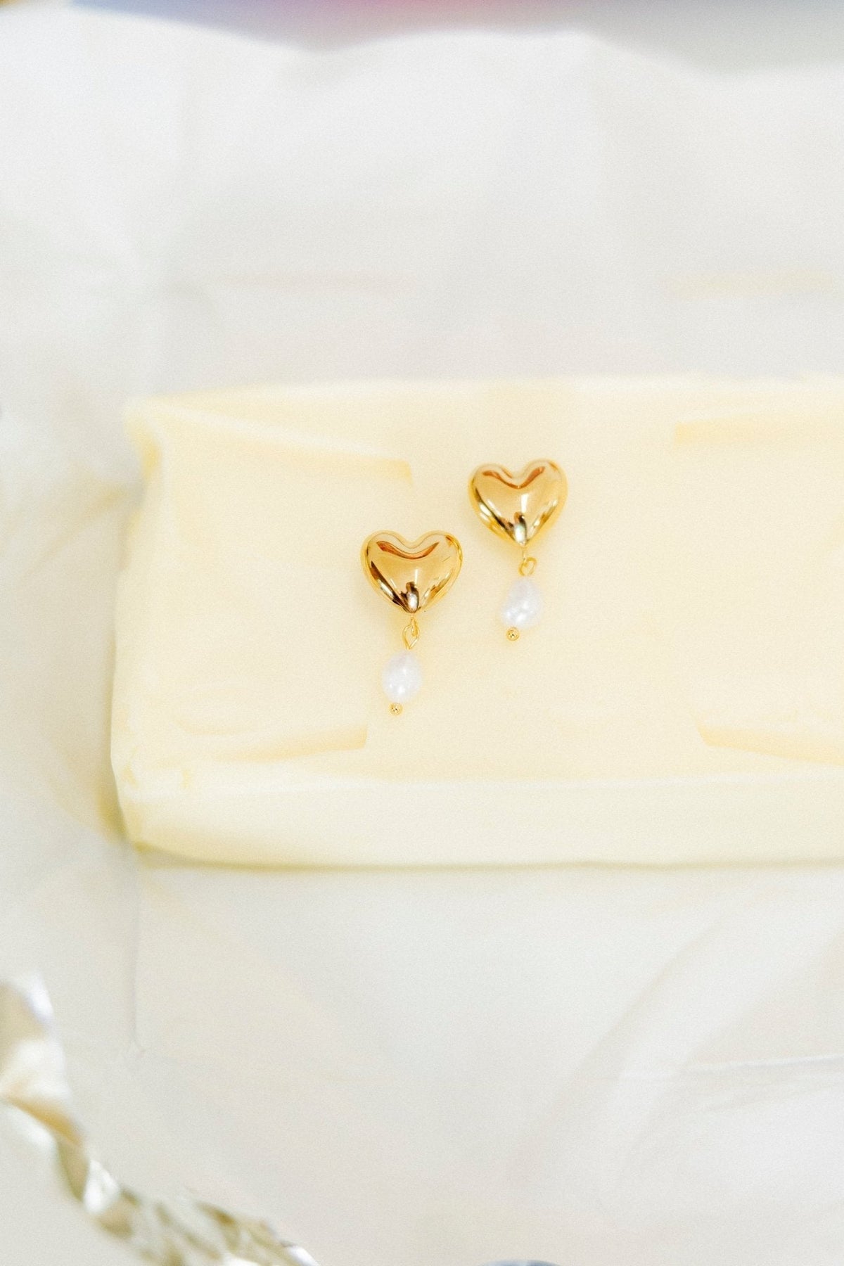 Gold-tone heart dangle earrings with pearl drops, displayed on folded tissue.