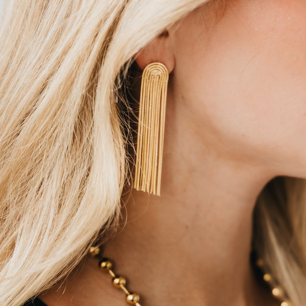 Gold tassel earrings with multiple chain strands, worn on an ear