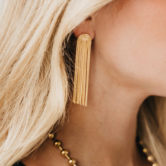 Gold tassel earrings with multiple chain strands, worn on an ear