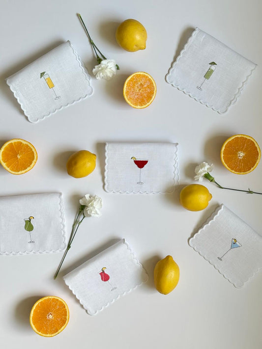 Set of 6 cocktail napkins with embroidered drink icons, white cloth and scalloped borders.