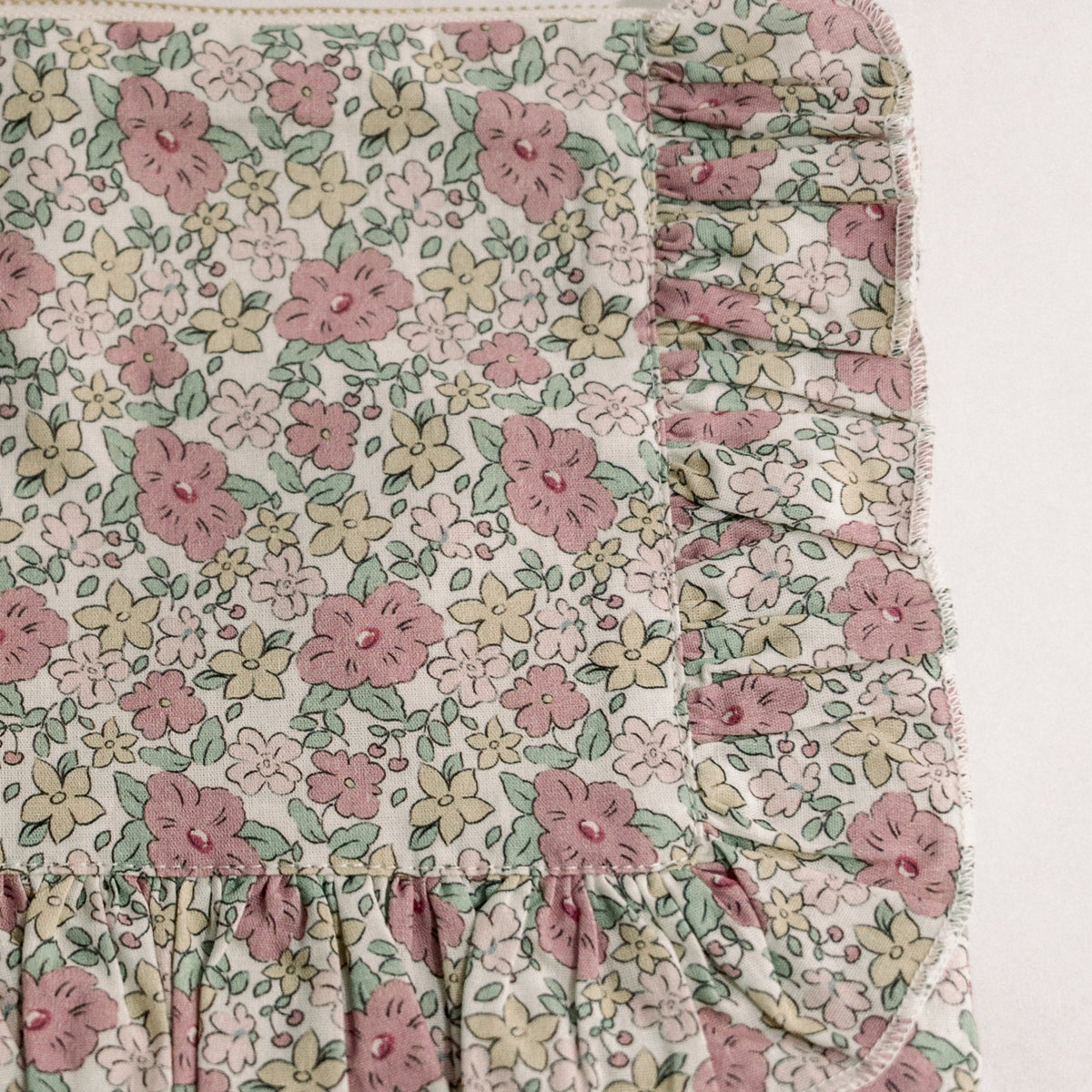 Close-up floral pouch panel with ruffle hem and partial zipper detail at top.
