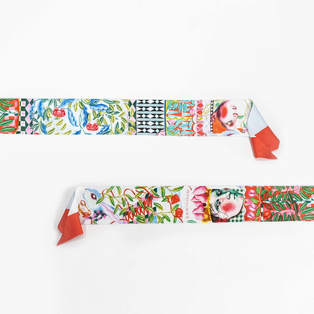 Silk twilly scarf laid flat, light blue illustrated borders with orange-red knot ends