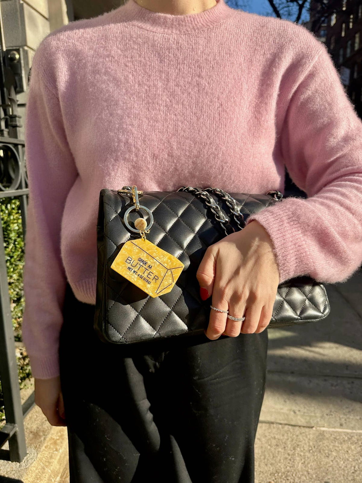 Butter bag charm keychain dangling on black quilted bag with gold hardware