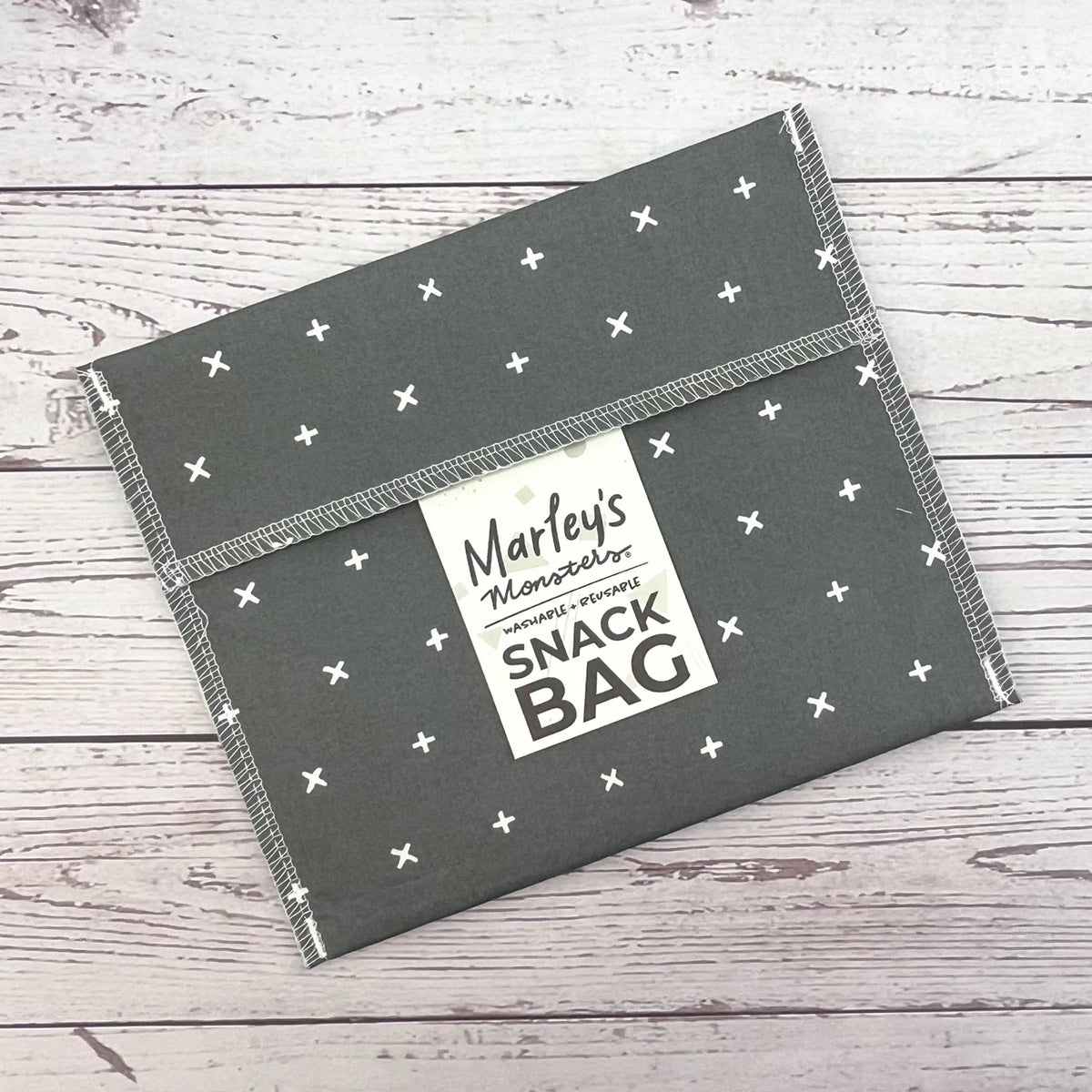 Reusable snack bag with dark gray fabric and white cross pattern, sealed top flap.