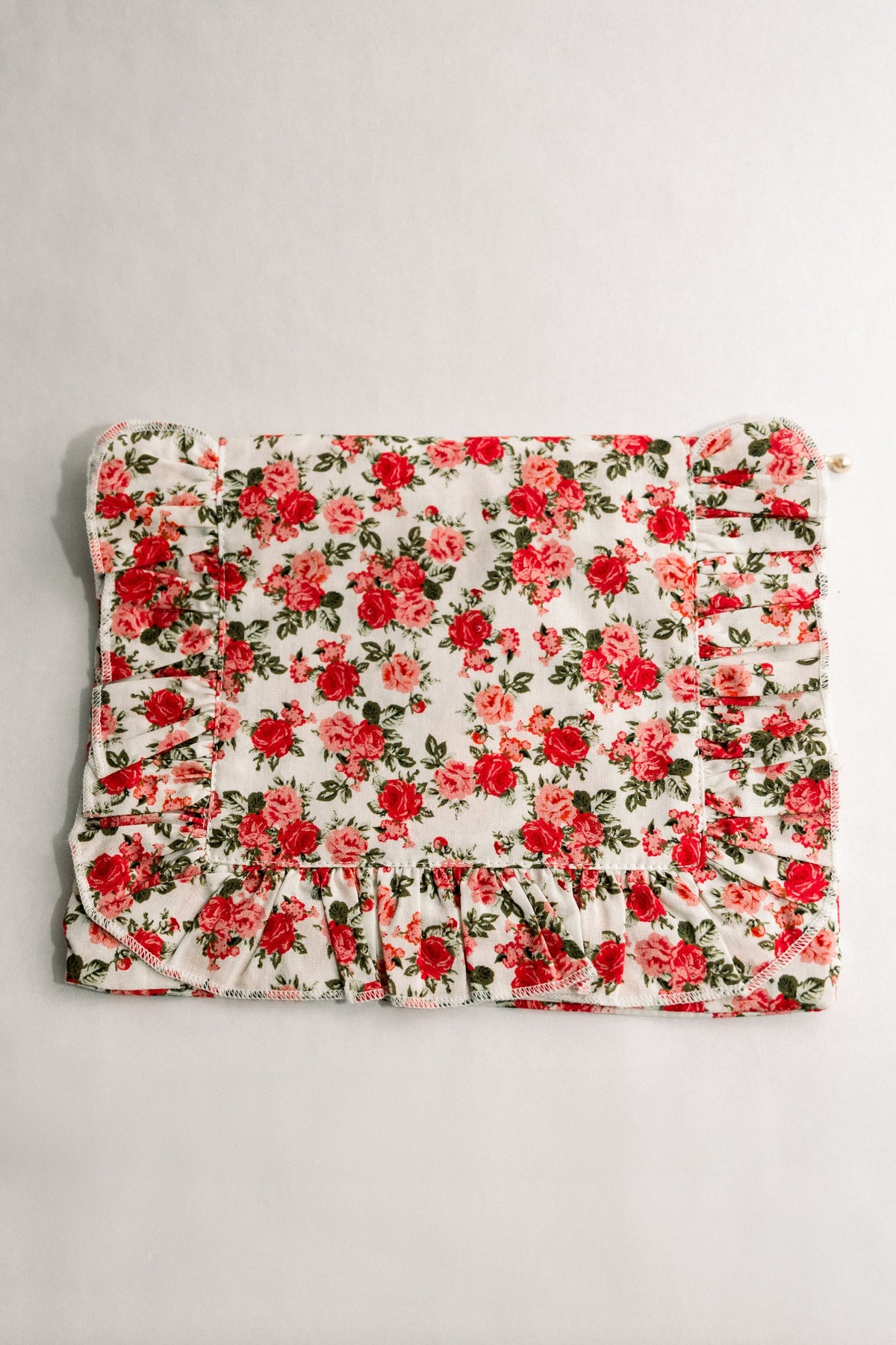 Floral ruffle zipper pouch with red rose print, gathered ruffle trim, and gold zipper pull