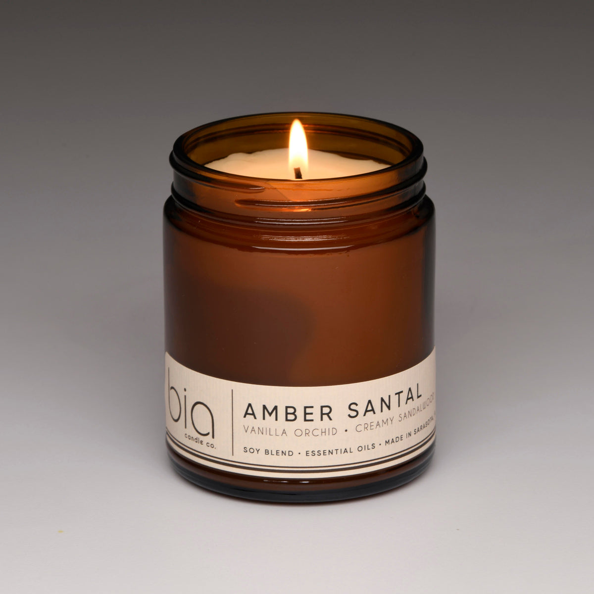 Amber glass soy candle jar close-up with flame and printed label
