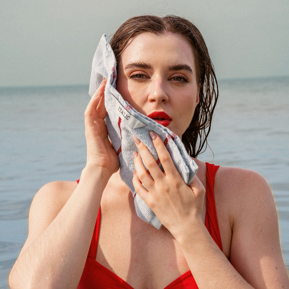 Light gray cotton towel with red stripes, held to face by hands