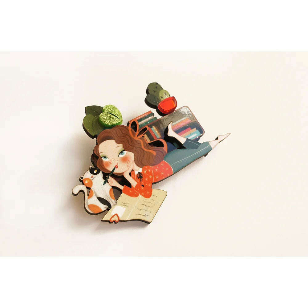 Laliblue diary brooch featuring illustrated girl reading, books, cat, and green hat