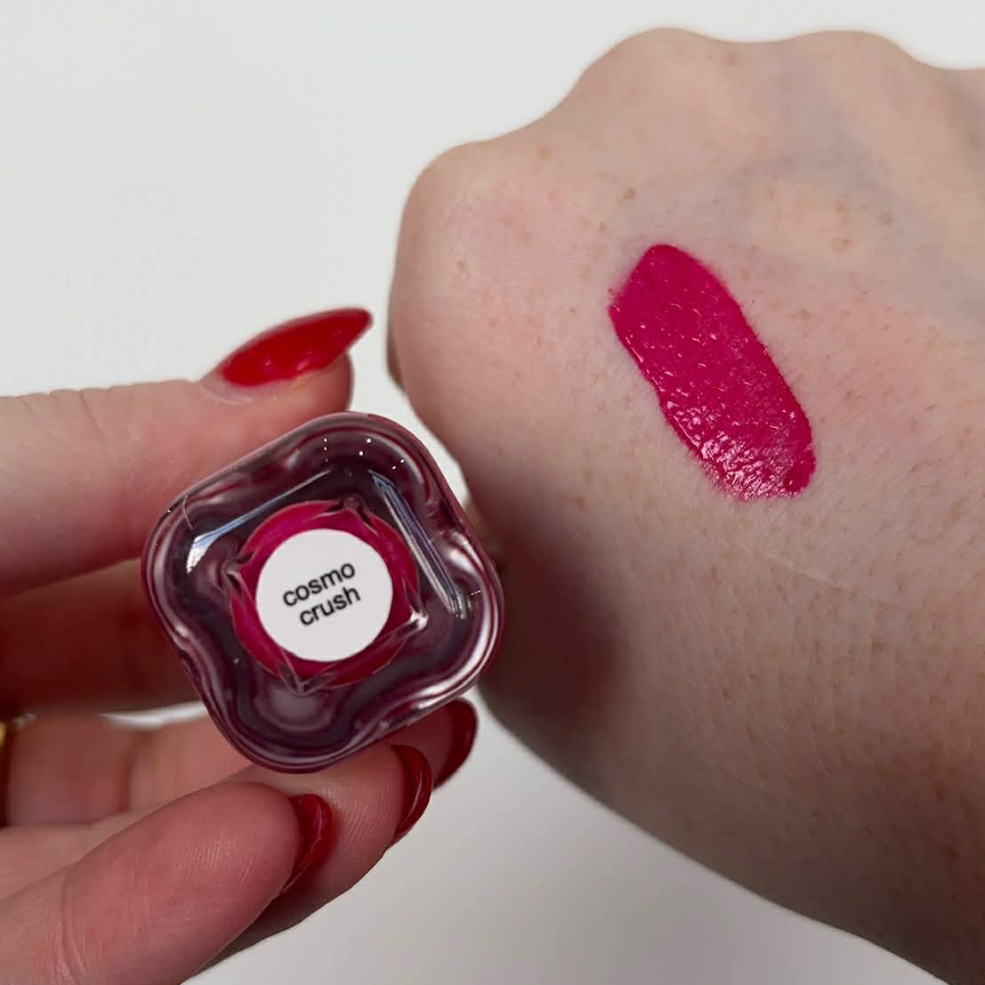 Liquid blush bottle with white cap next to a bright fuchsia swatch on the arm.