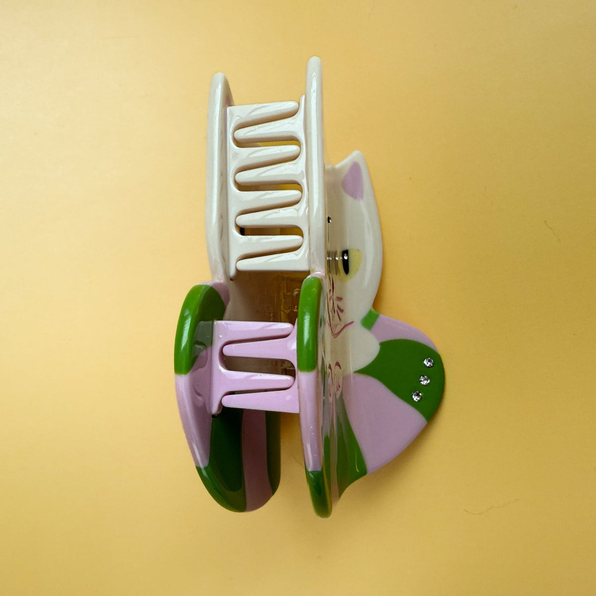 Cat hair claw clip side view with white comb teeth and green-and-pink accents