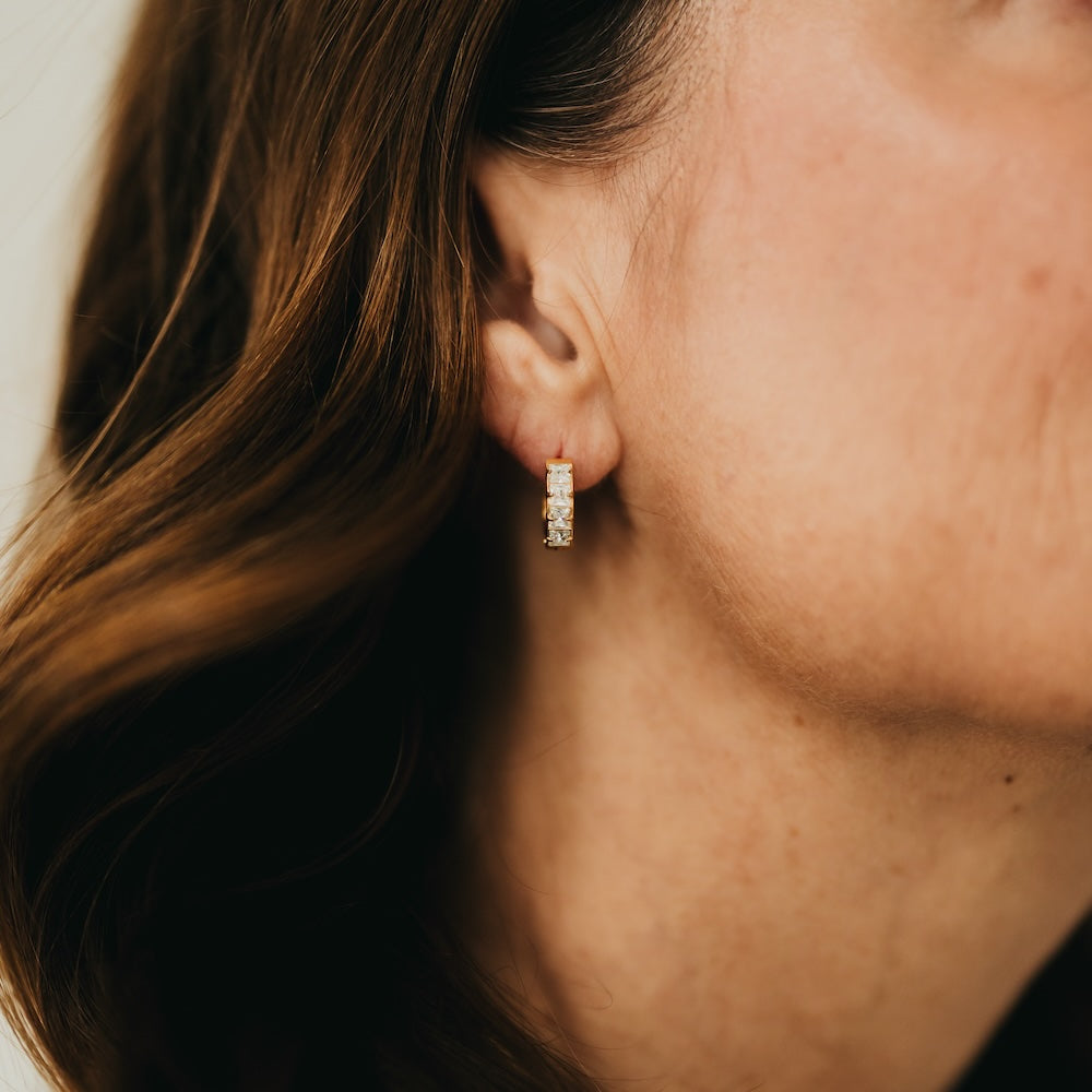 Gold huggie hoop earrings with small diamond-like stones, shown on ear