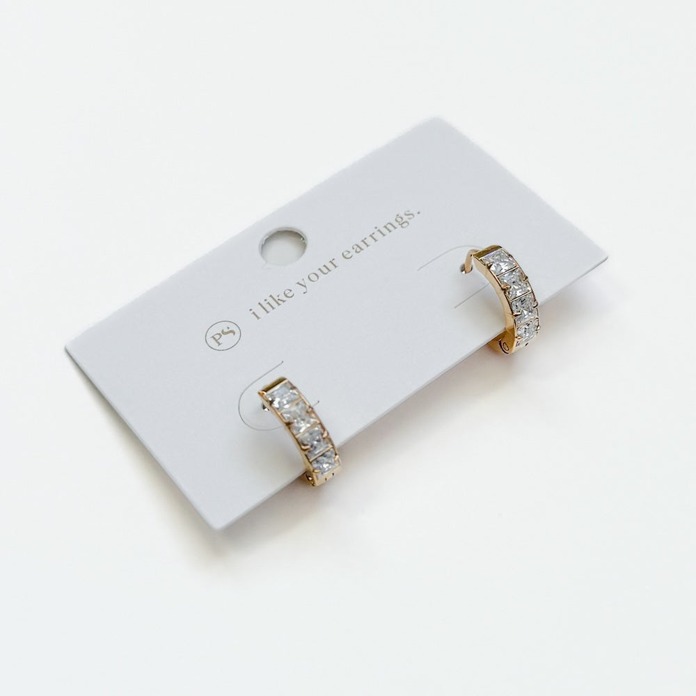 Gold huggie hoop earrings with diamond-like stones on a display card