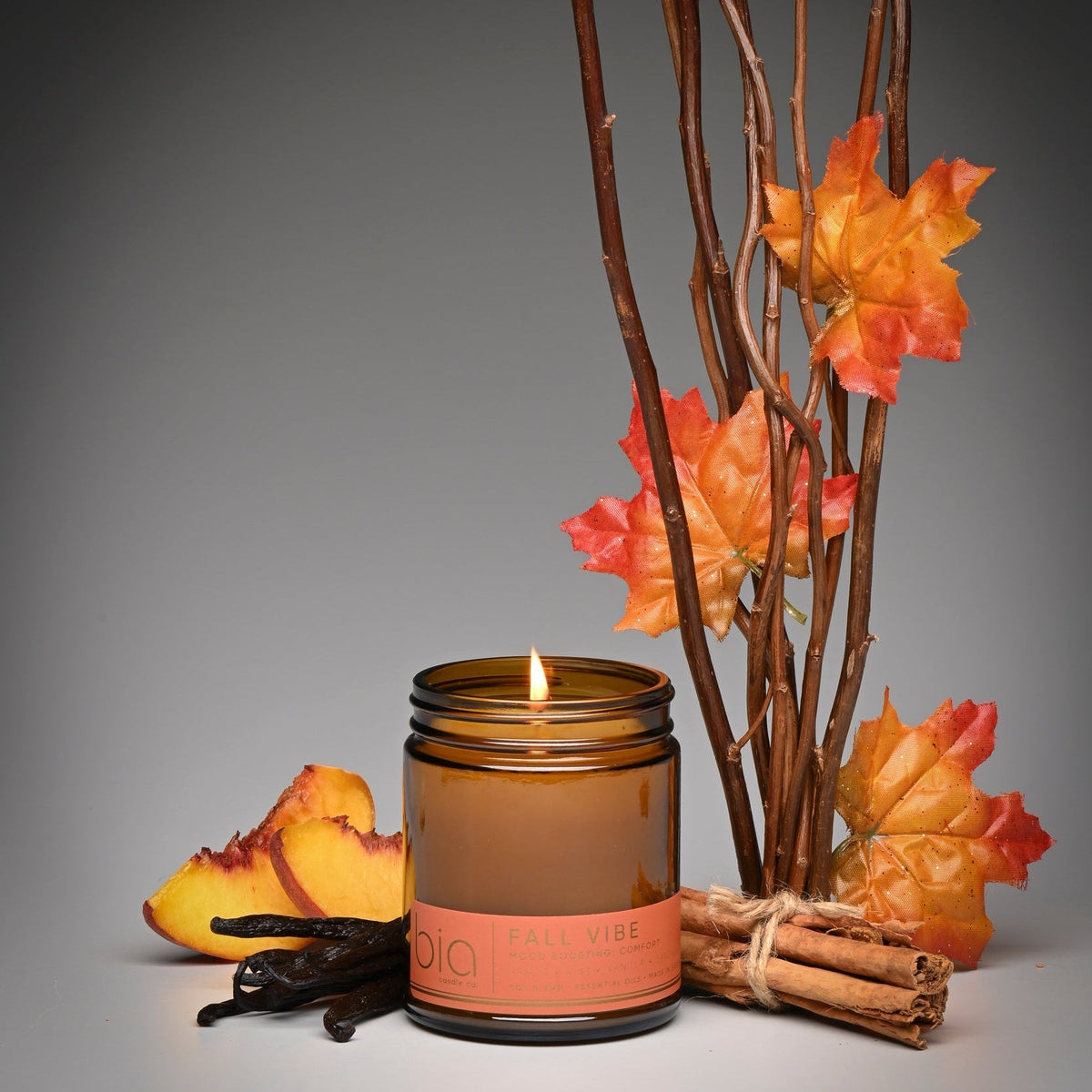 Amber glass soy blend candle with lit wick, 'bio' label, and orange maple leaves