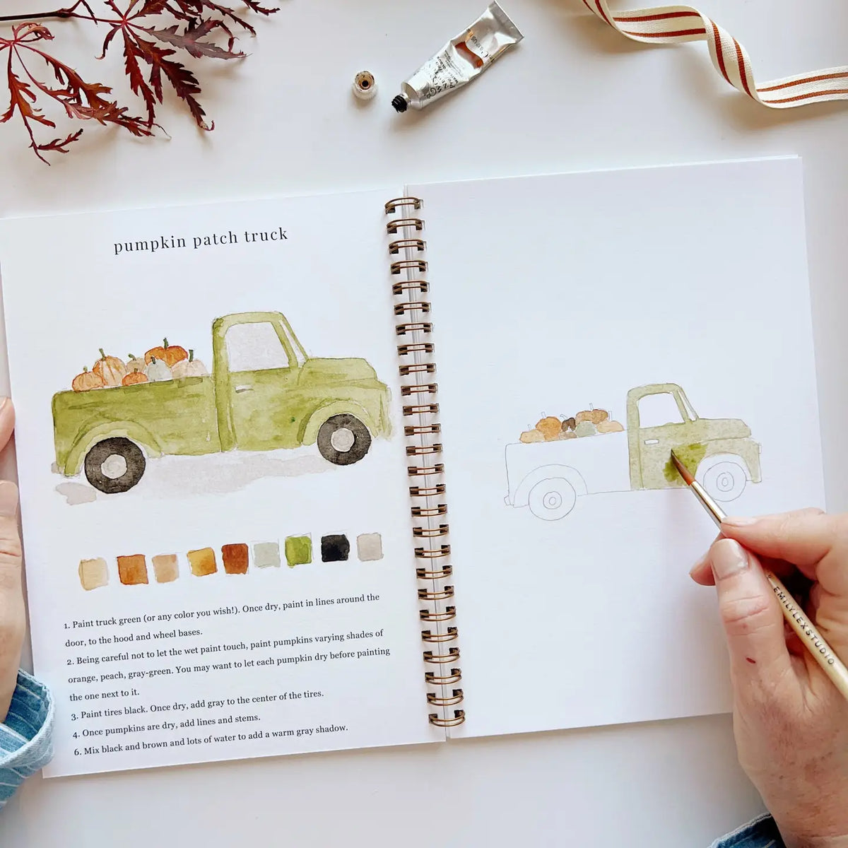 Open watercolor workbook with pumpkin patch truck illustration and paint swatch squares