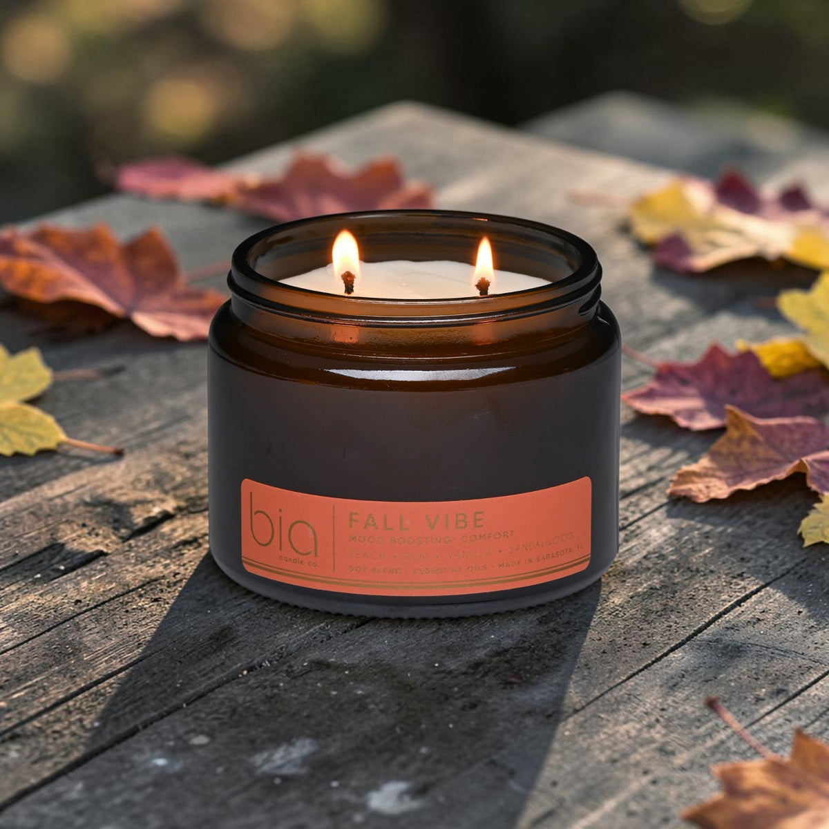 Amber soy blend candle with lit wick and 'bio' Fall Vibe label, surrounded by leaves