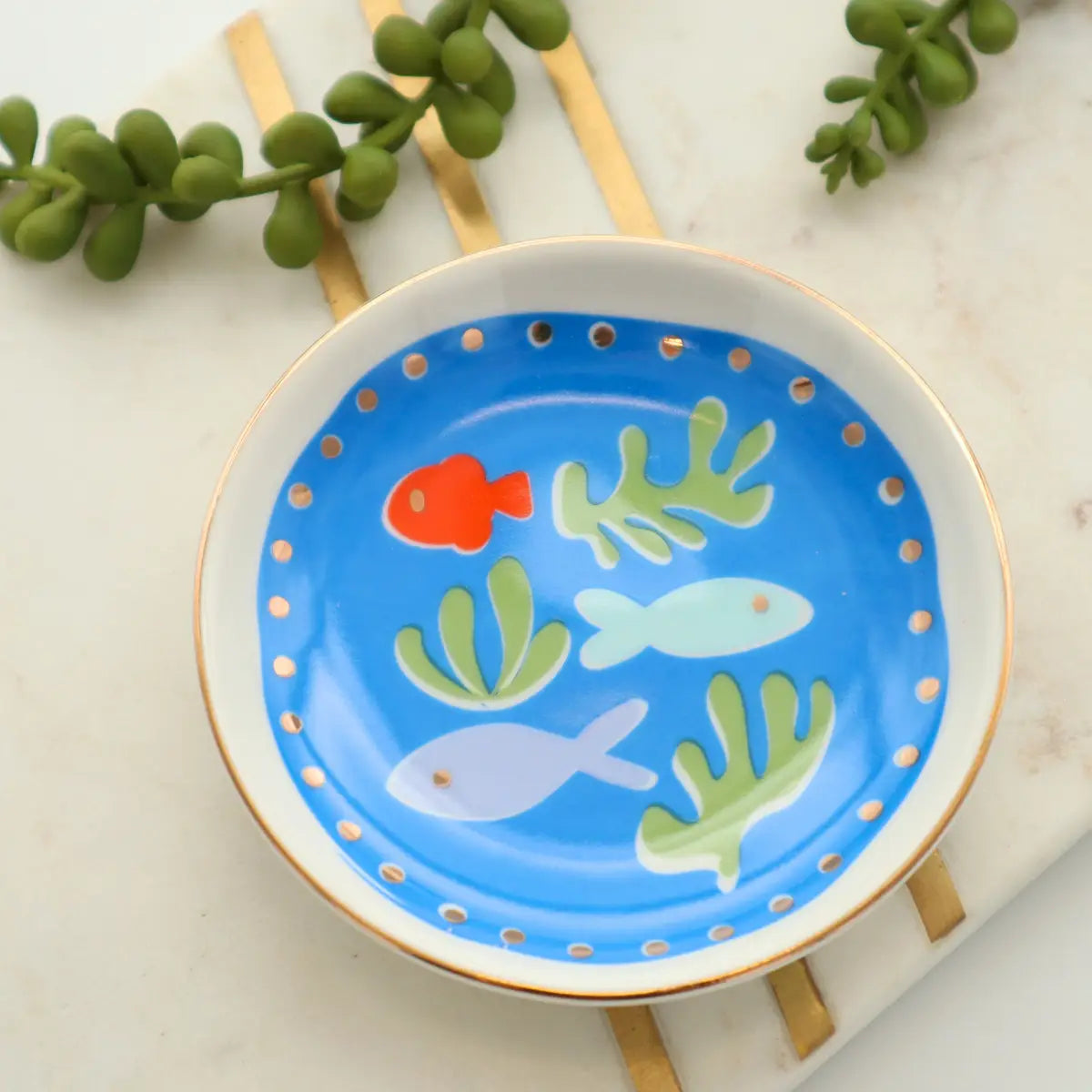 Round trinket tray with a blue fish and seaweed design, gold rim, and dotted border